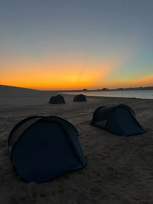 Barracas do camping na areia com o céu alaranjado do fim de tarde