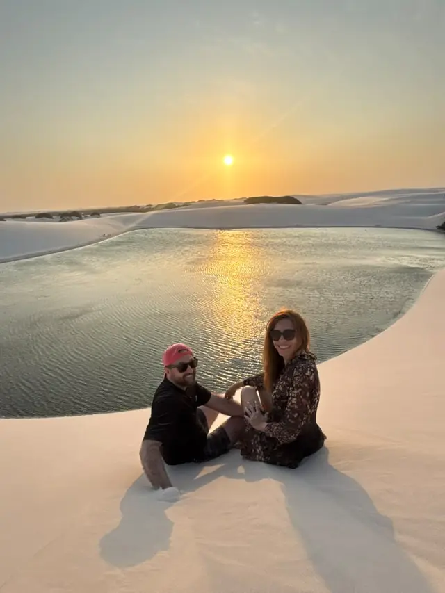Casal sentado na duna com o reflexo do pôr do sol na lagoa