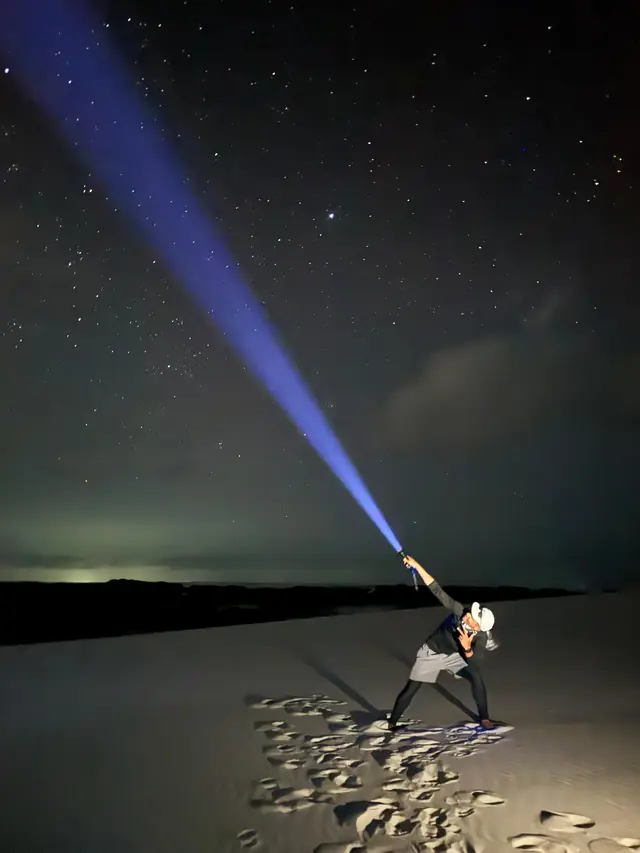 Guia iluminando o céu noturno com uma lanterna sobre as dunas